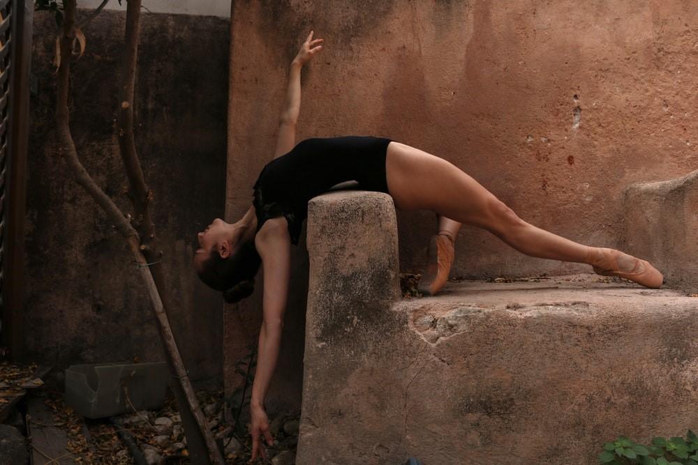 A ballerina bending her body over a brown rock