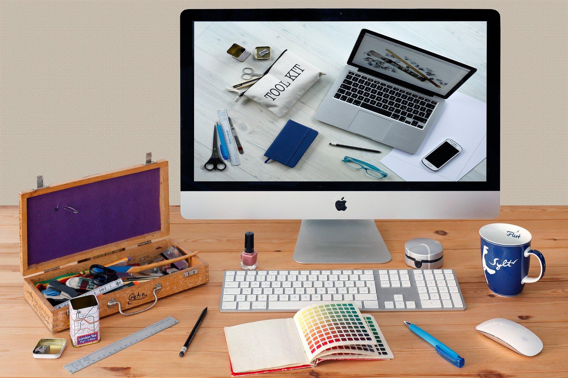 An iMac on a table with creative designer's tools in the foreground