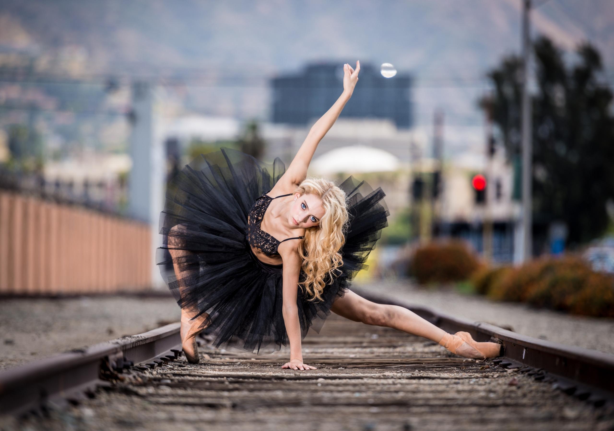A female ballerina in a black tutu dress posing for a picture on a railway