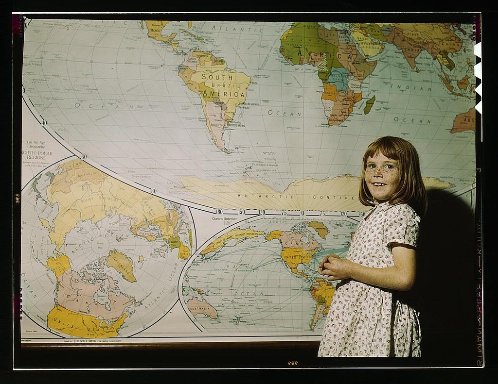 A child posing next to a huge poster of the world map