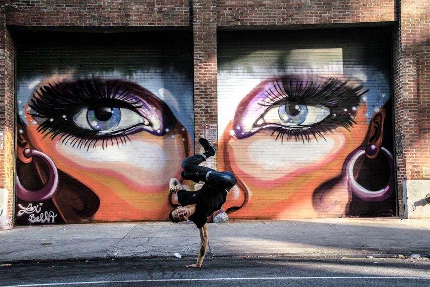 A breakdancer dancing in front of a wall with graffiti art