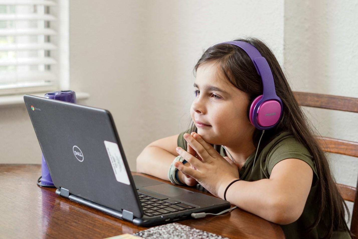 A girl with pink and purple headphones on, looking at her laptop screen