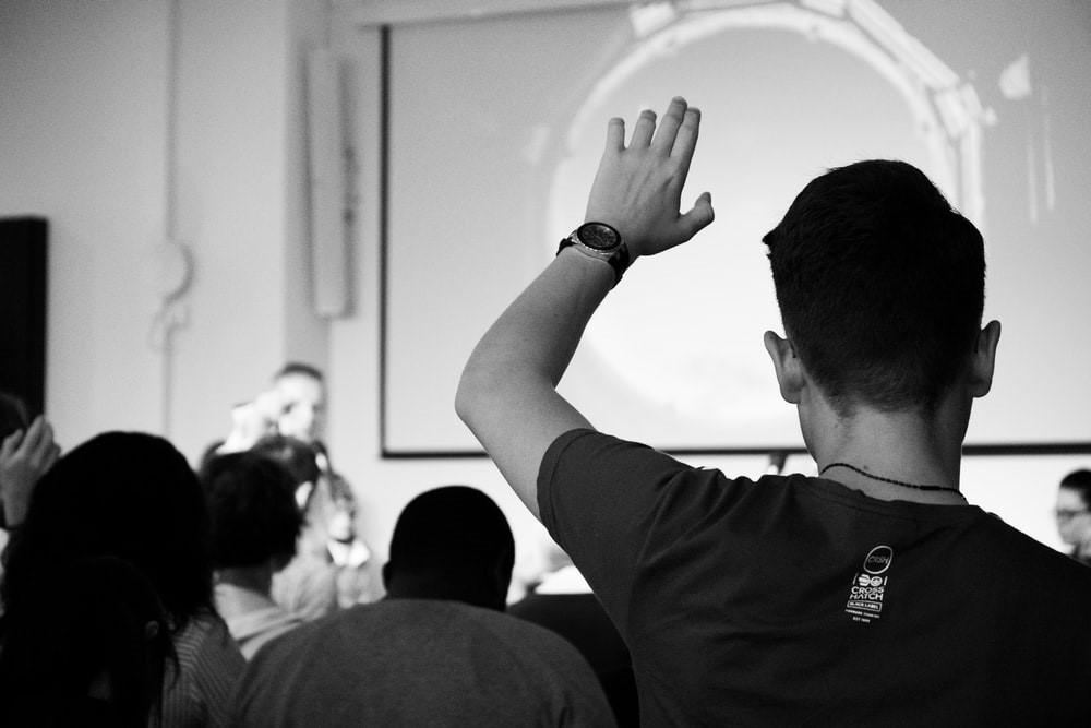 A student wearing a black t-shirt raises his hand to ask a question from his chemistry professor