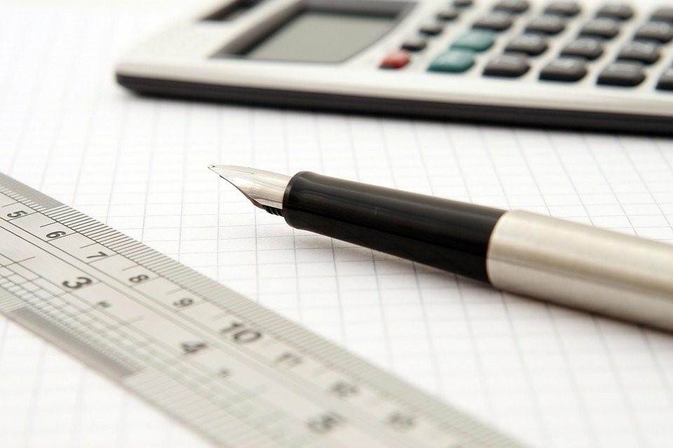 A pen is placed on a notebook besides a calculator and ruler