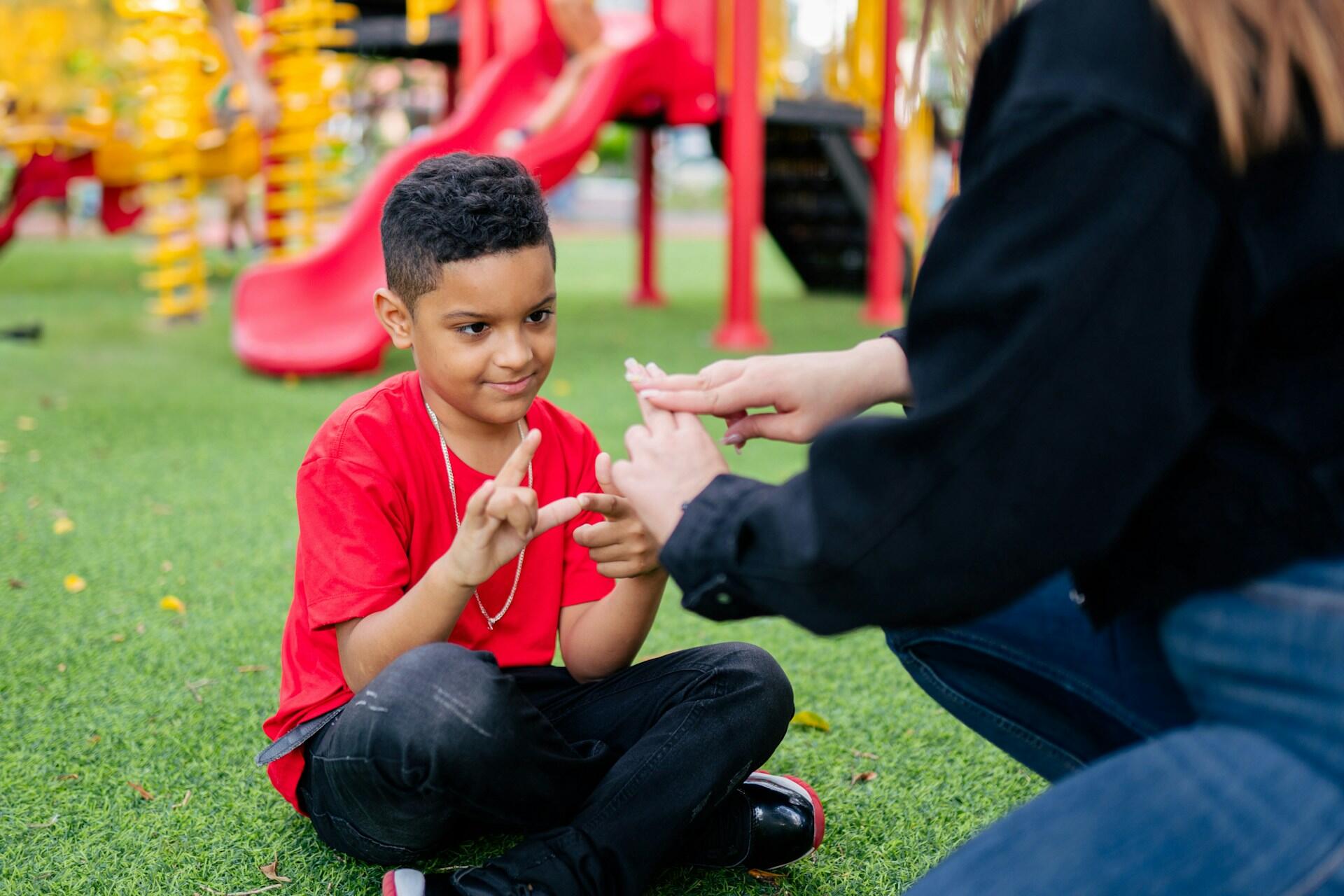 A young boy learning sign language in a park.