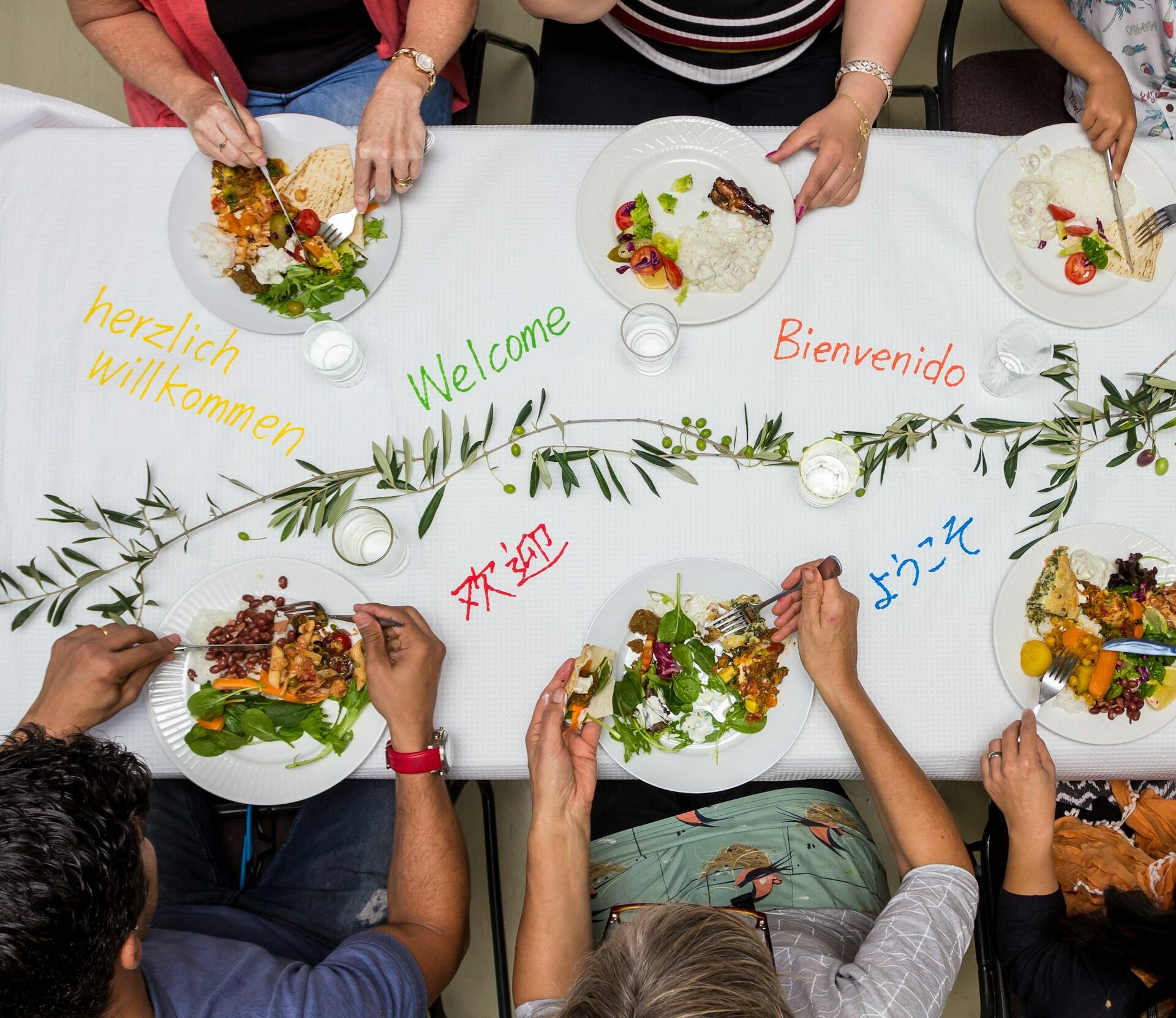 a table with several people eating from plates. the tablecloth has "hello" written in several languages on it