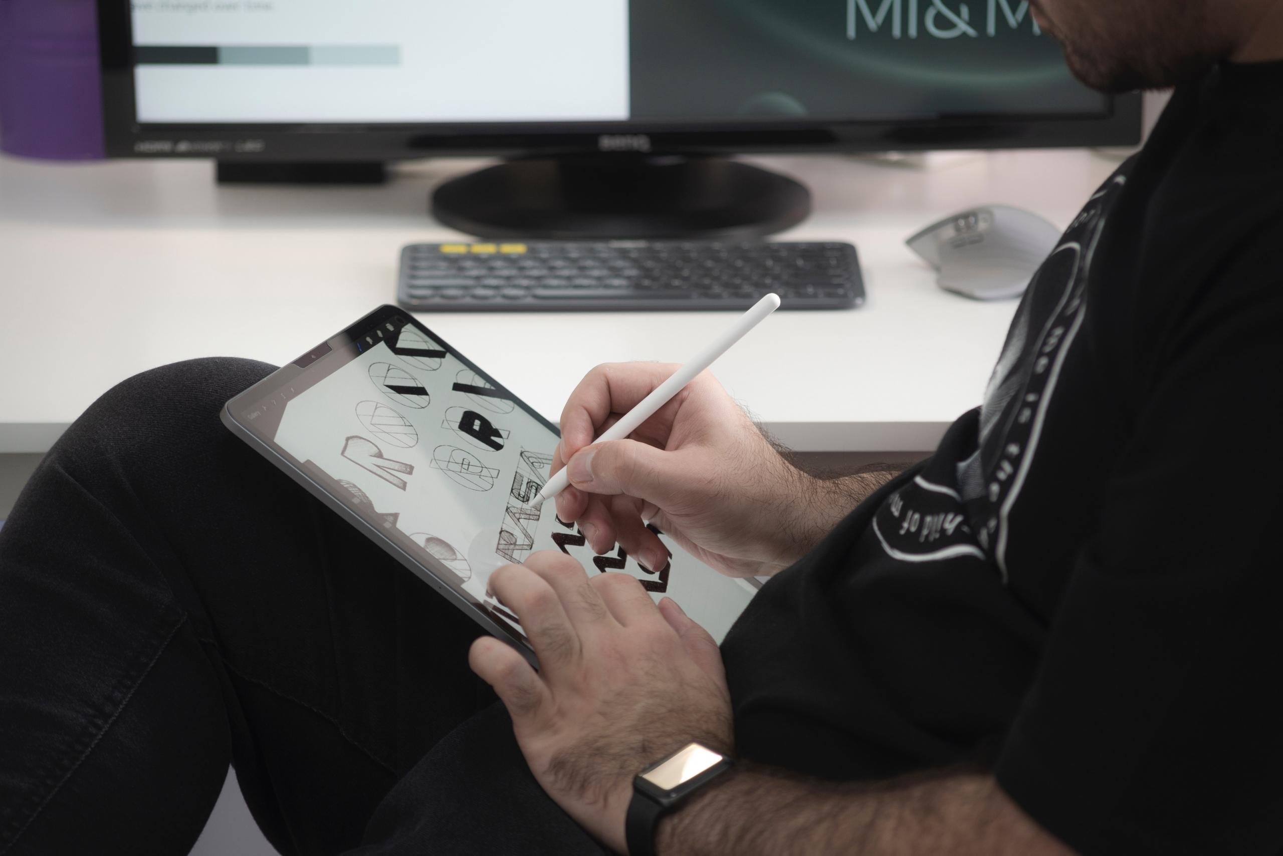 A person in a black jacket holding a tablet doodling alphabets.