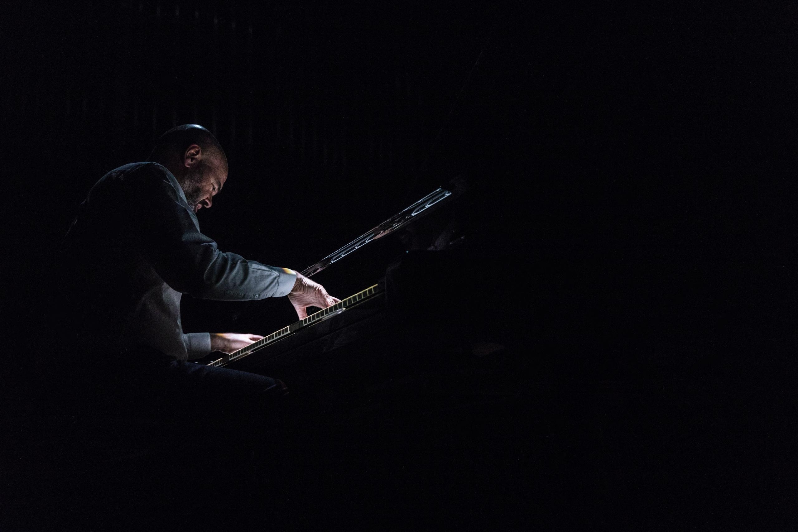 Man playing the piano with one light iluminating him.