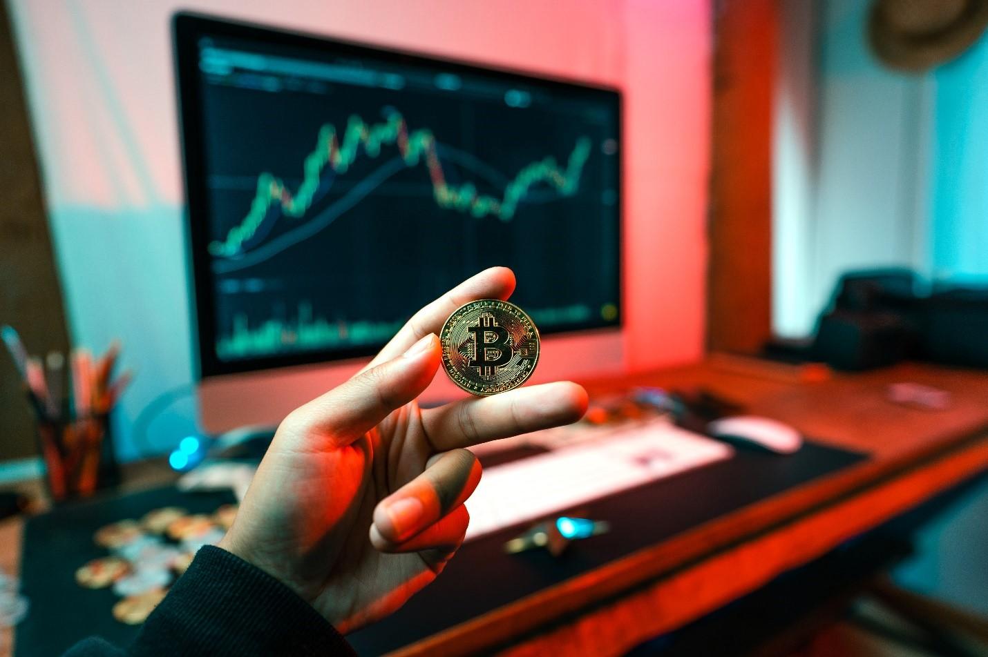 A person holding a physical Bitcoin in front of their computer screen