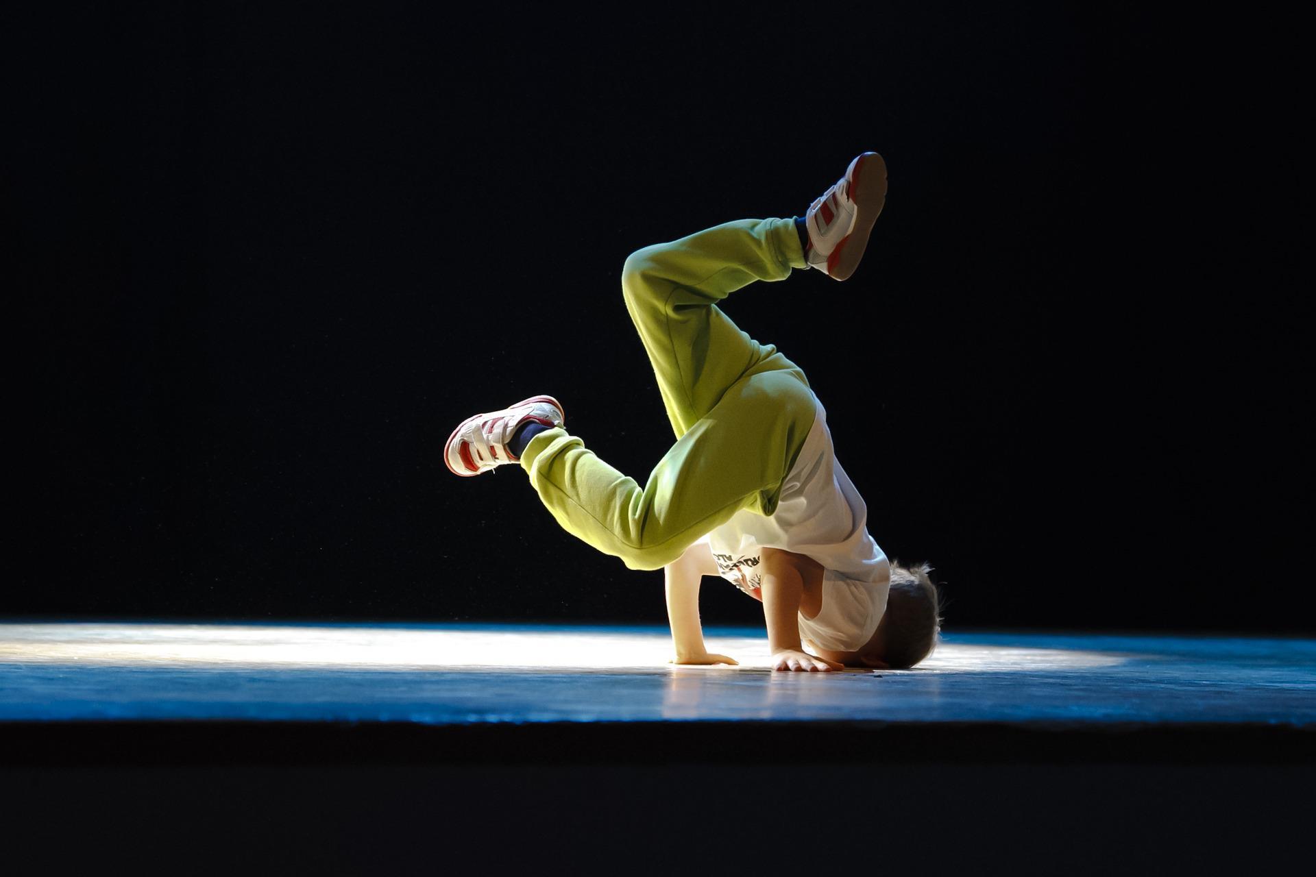 Boy wearing a white t-shirt and green pants and showing hip hop dancing skills