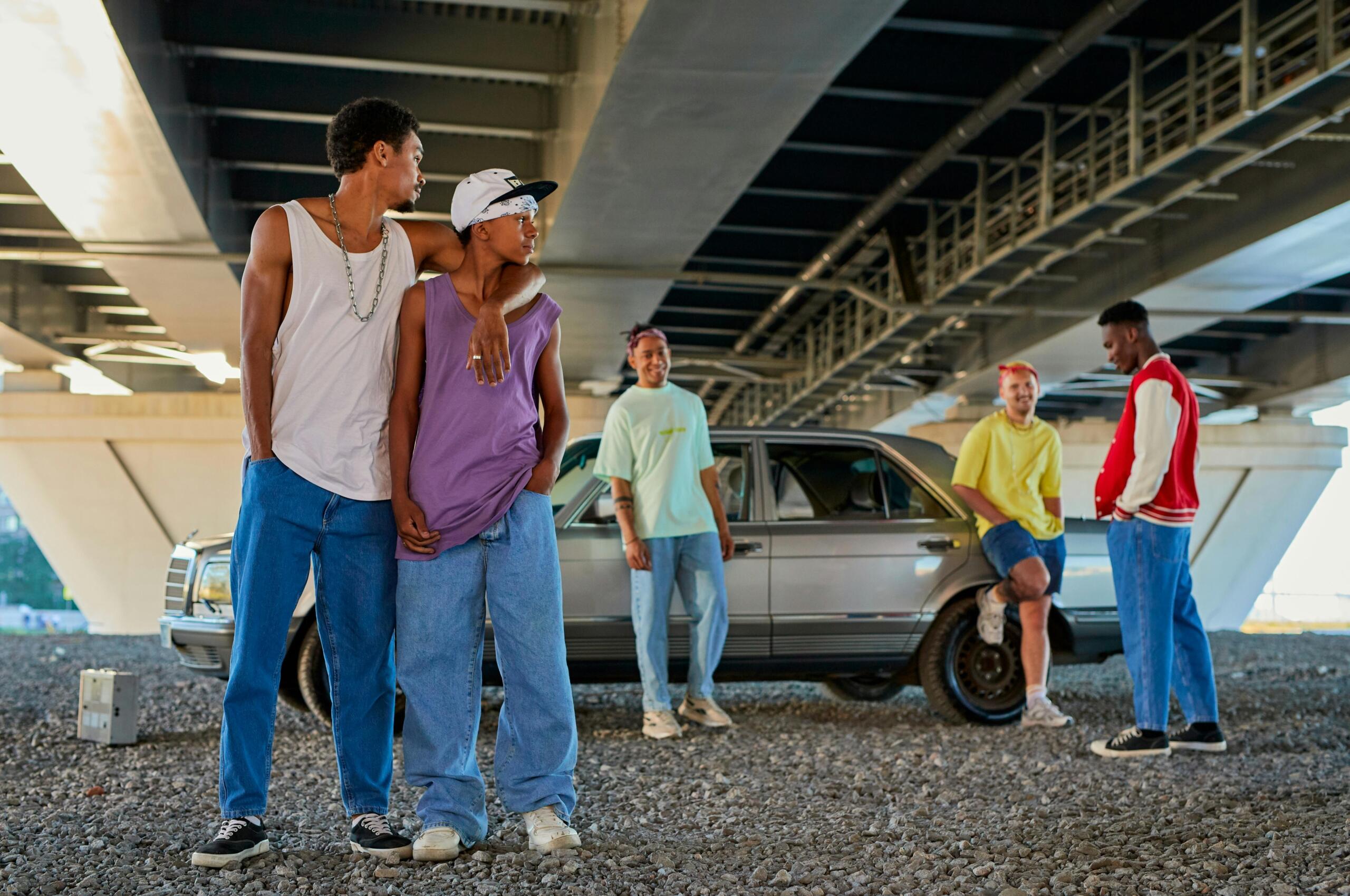 A group of men standing under a bridge, dressed in urban streetwear.