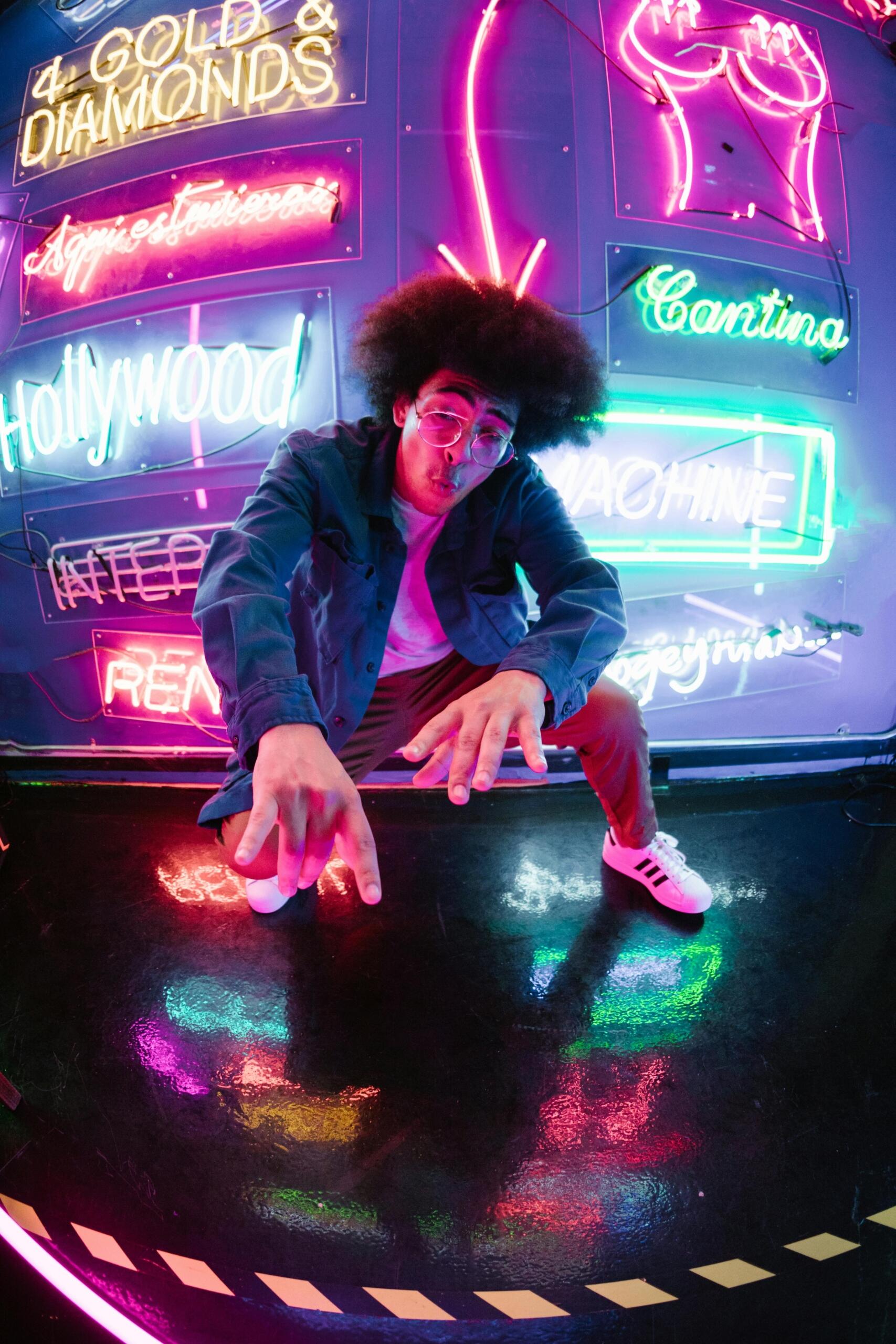 A man posing beside a wall illuminated by vibrant neon lights in an urban setting.