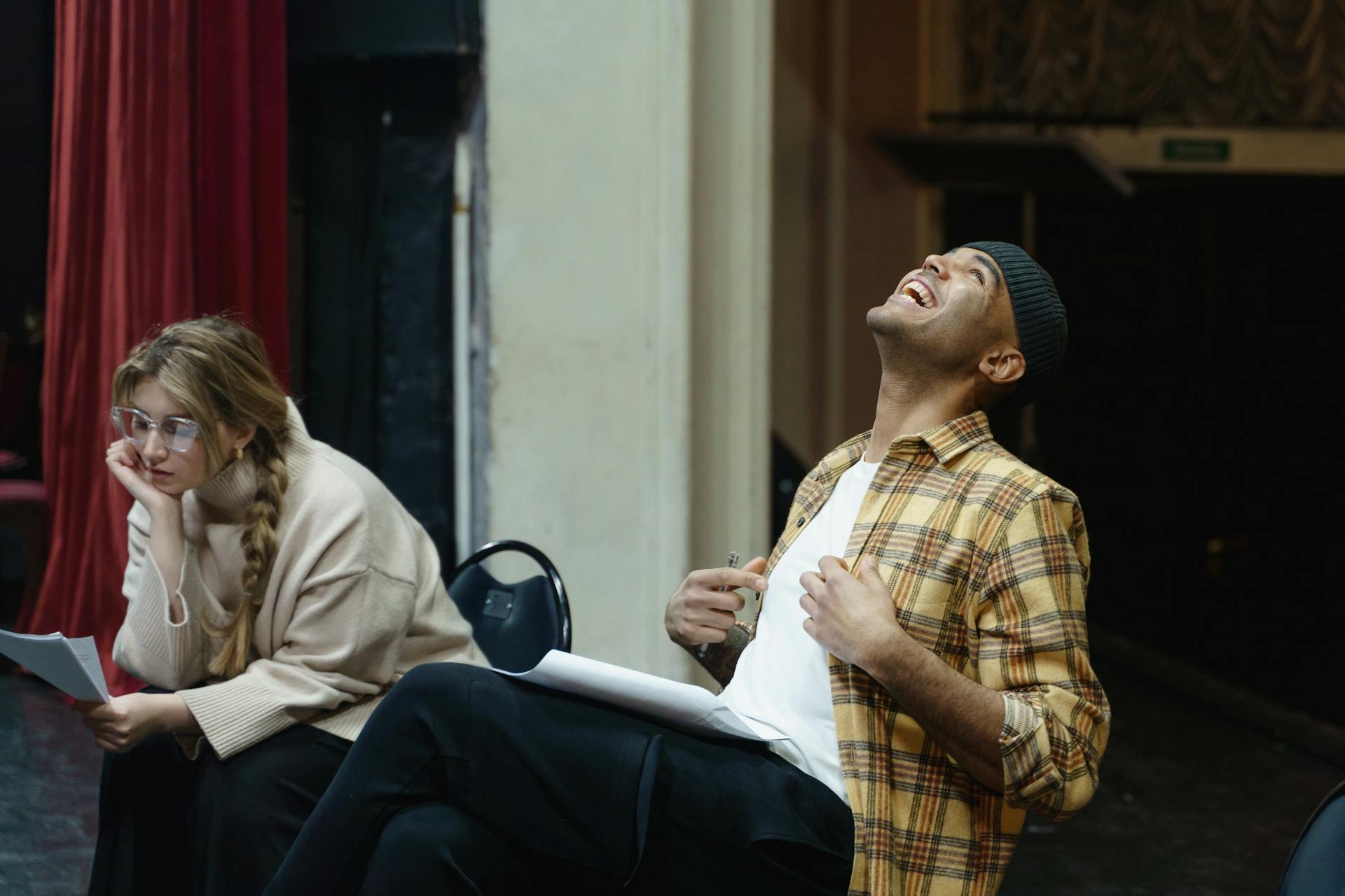 A girl and guy sitting, and the guy laughing