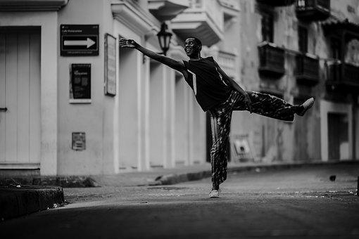 A black man dancing in the middle of a street with buildings surrounding him in a monochrome setting