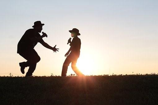 A young kid dancing and singing with an older man on a field during sunset