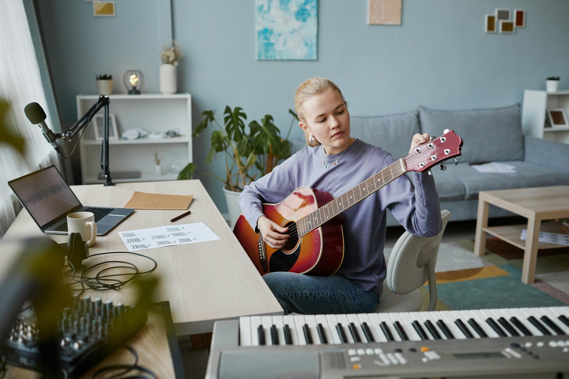 A girl sitting at her desk, tuning her guitar.