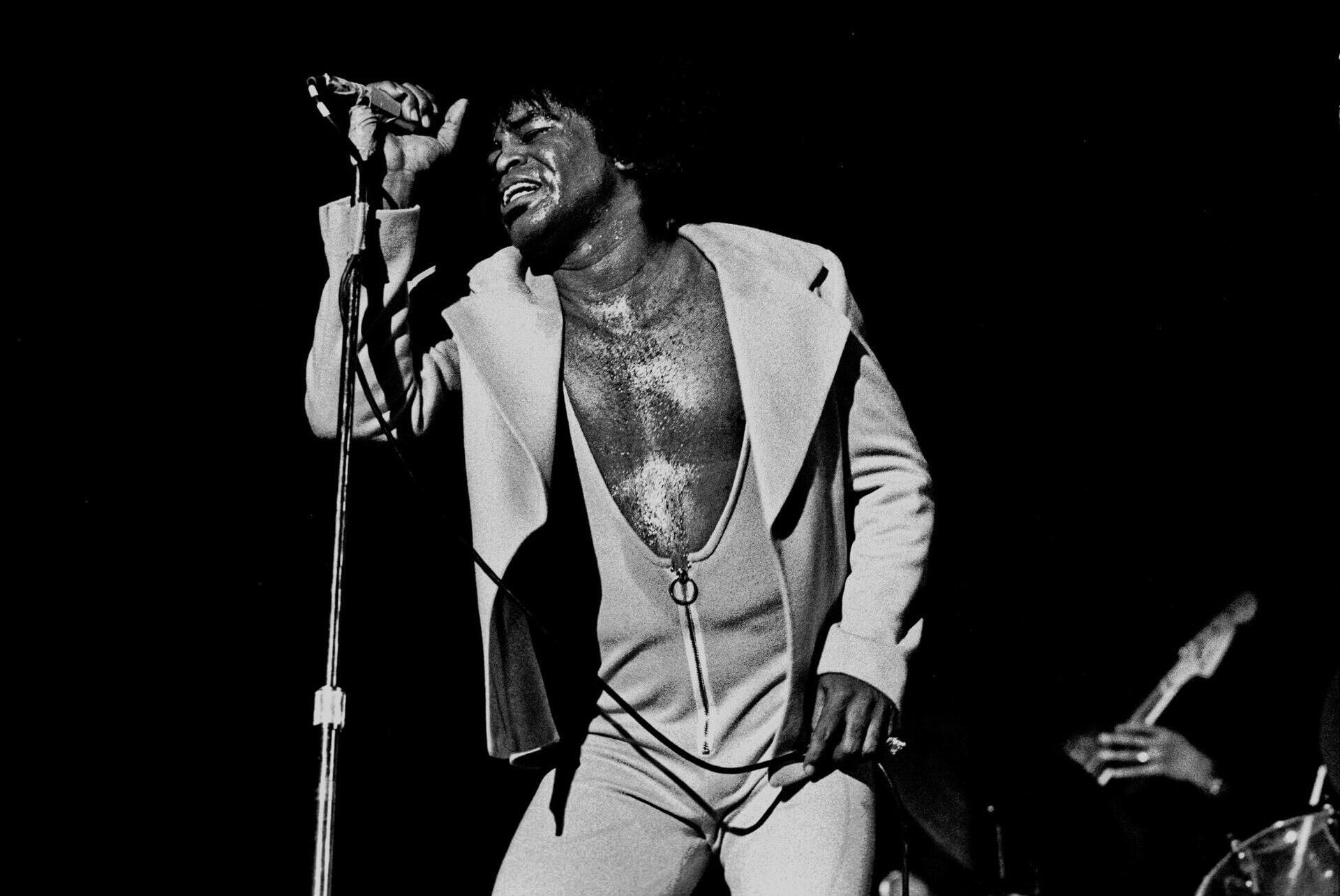 James Brown holding a microphone and singing on stage.