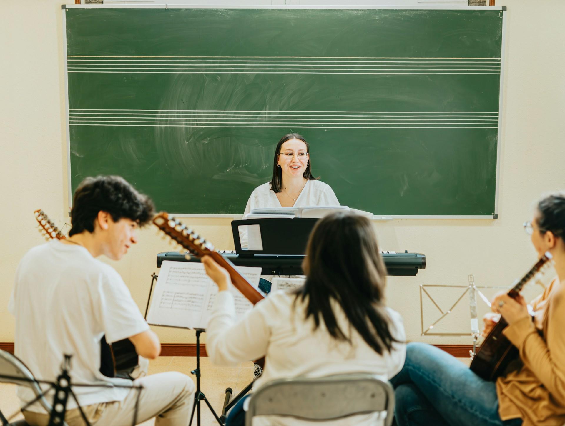 A tutor in a classroom giving music and singing lessons to three students.