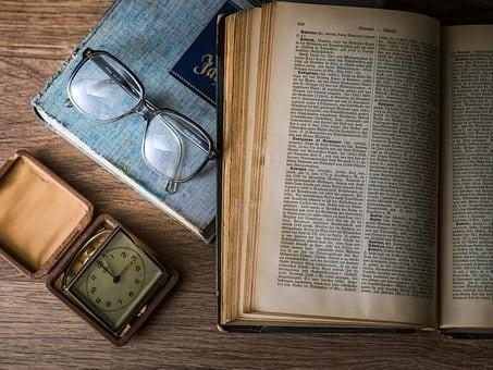 A literature book lies open with a pair of classes and a pocket watch