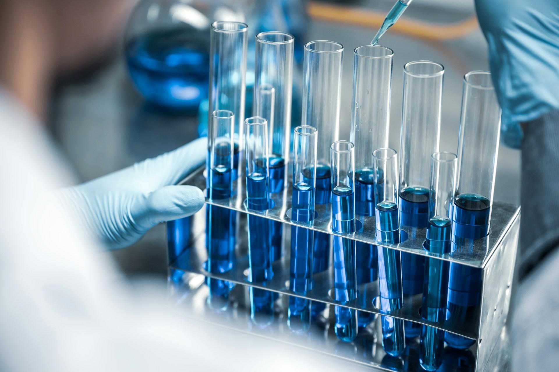 A scientist working with test tubes and blue liquid