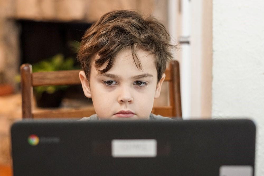 Kindergarten student looking at a laptop computer while participating in distance home learning