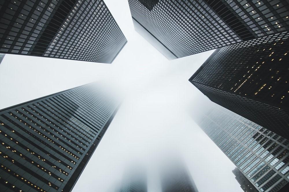 Low-angle photography of grey skyscraping buildings with glass windows and golden fluorescent light bulbs.