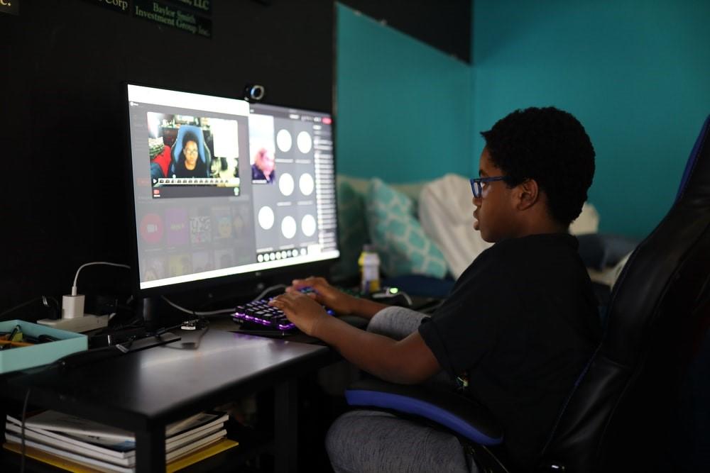 Boy with glasses on sitting in his room, attending an online class.