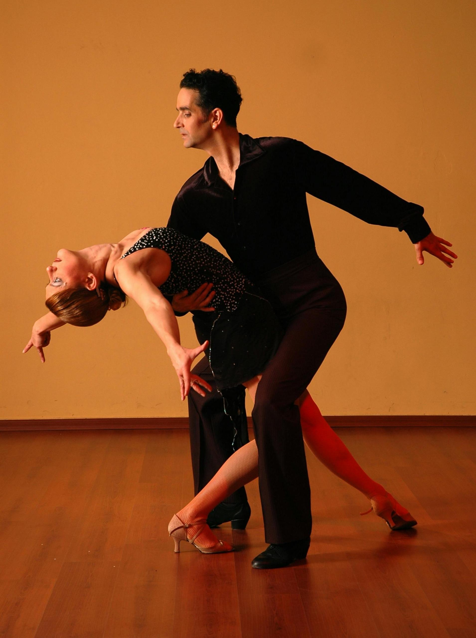 Two salsa dance partners in action, with one partner bending while the other leads with an elegant pose.