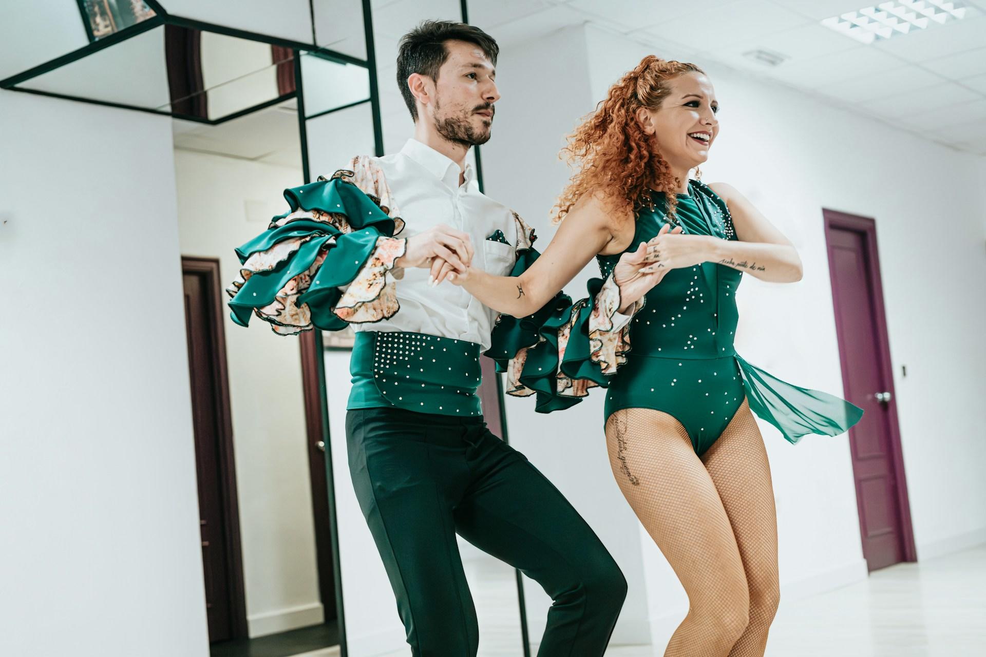 Two people in green dancing outfits dancing the salsa.