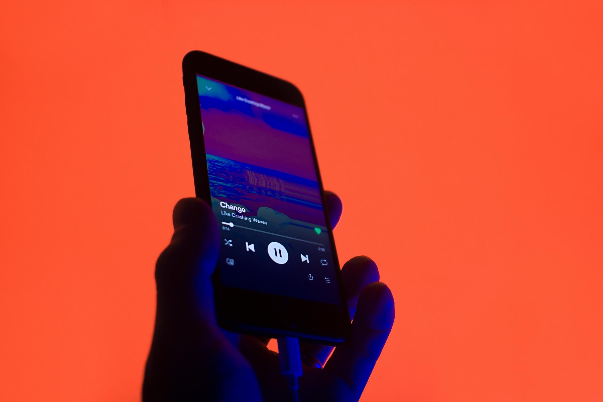 Spotify music playing on a phone over an orange background