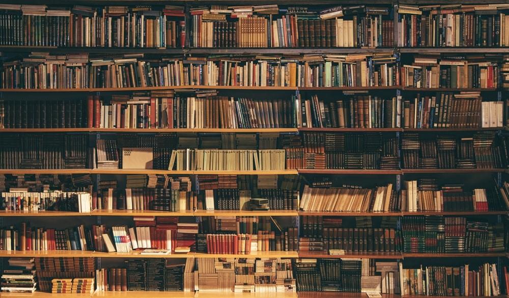 Hundreds of color-coordinated books and novels on various bookshelves in what seems like a library.