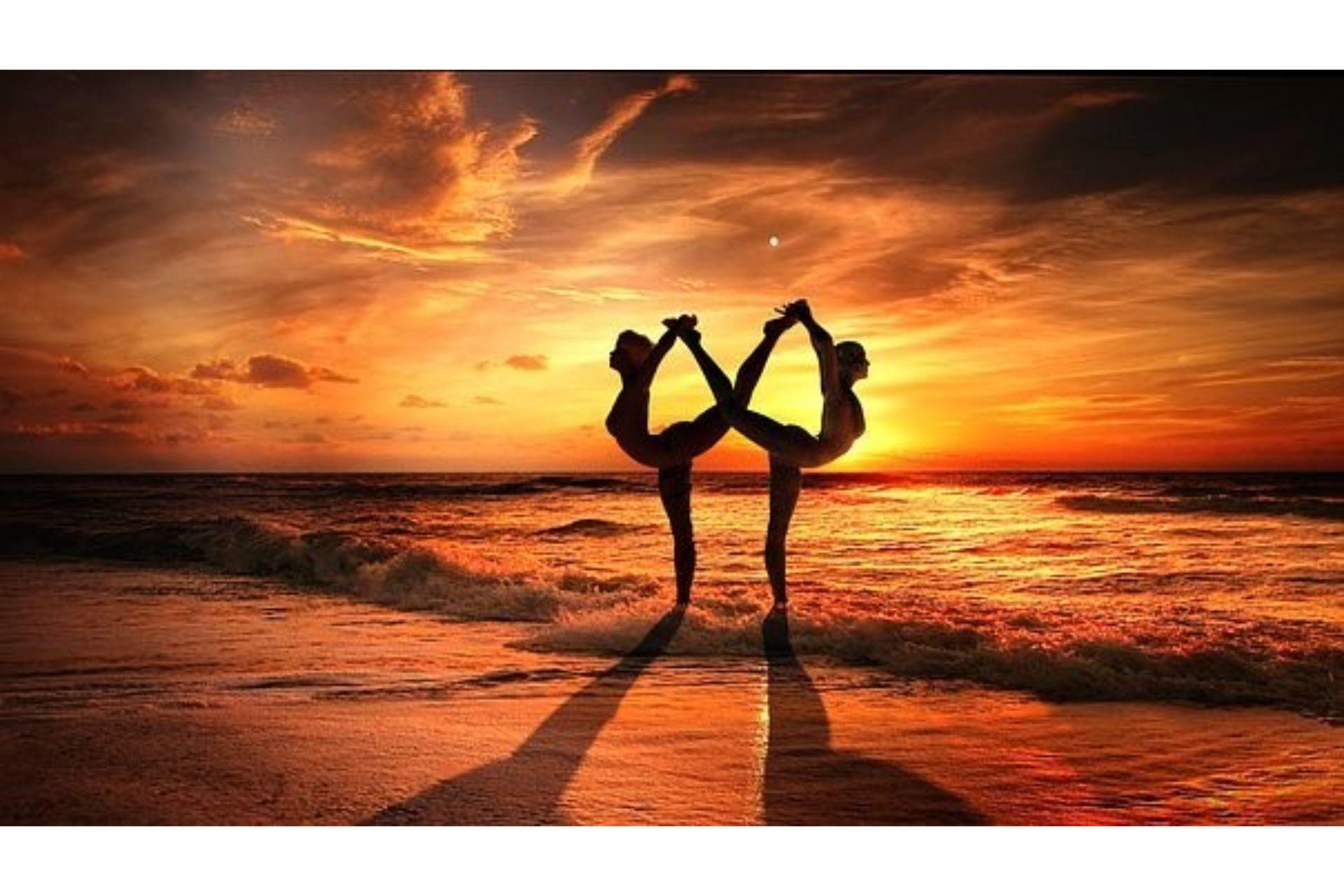 Two women practicing AcroYoga at a beach.