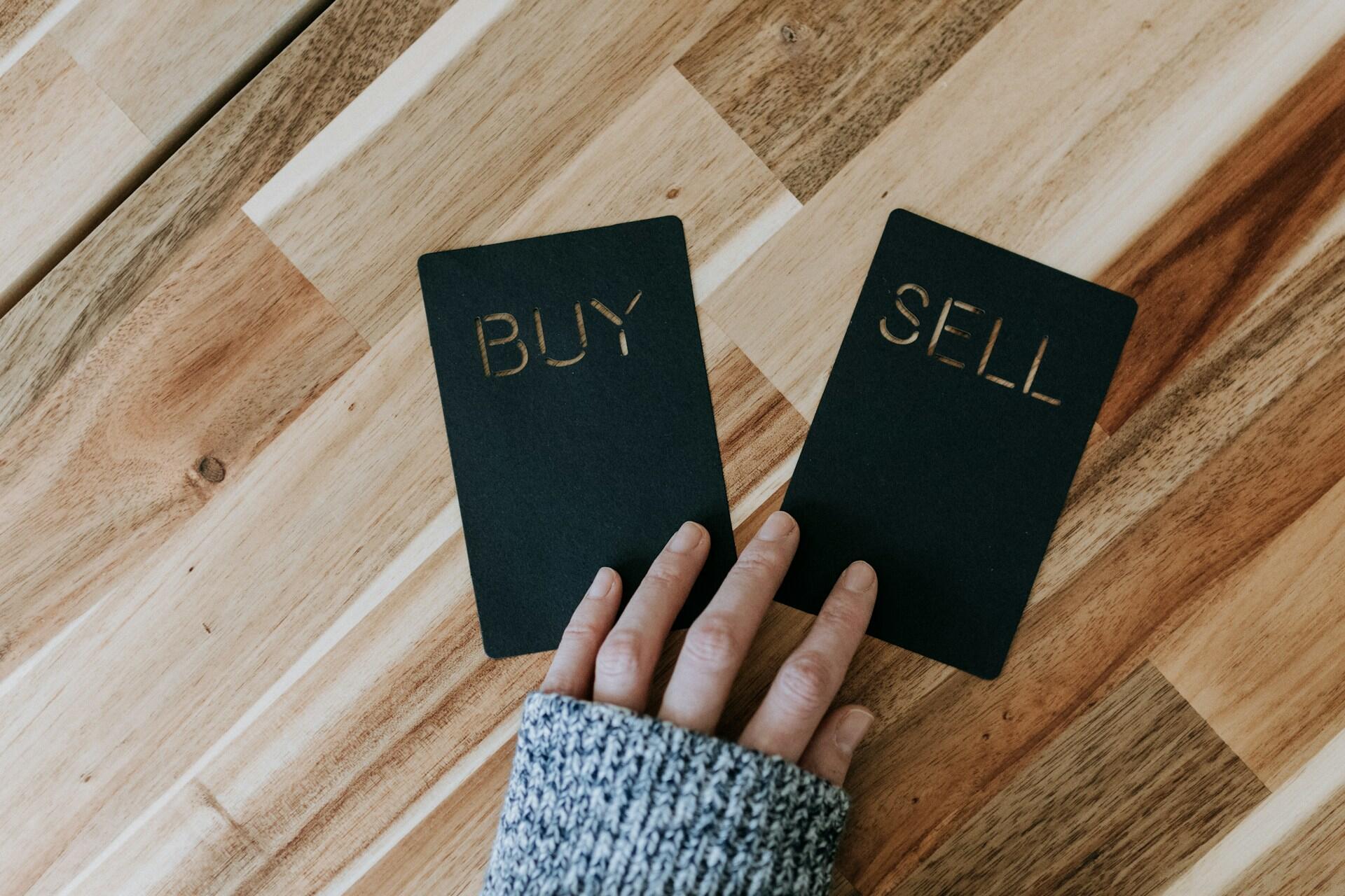 A person holding two cards, one labeled "buy" and the other labeled "sell".