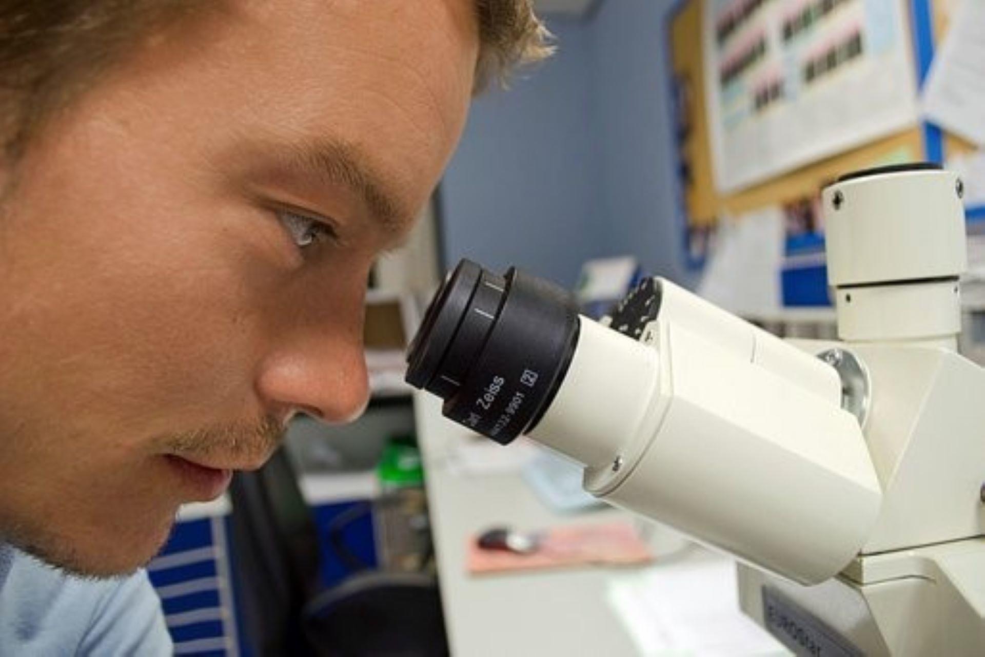 A chemical analyst examining a lab specimen using a microscope