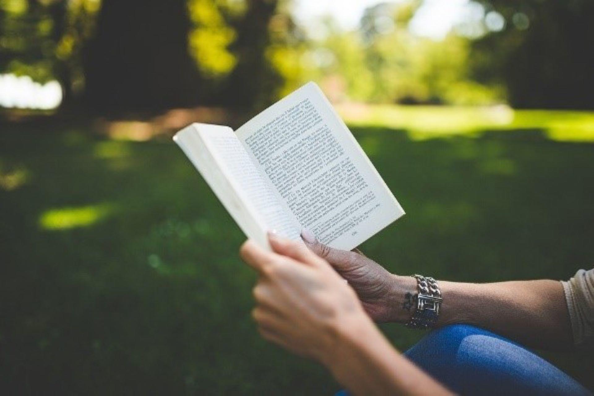 A person reading a book on a lawn.