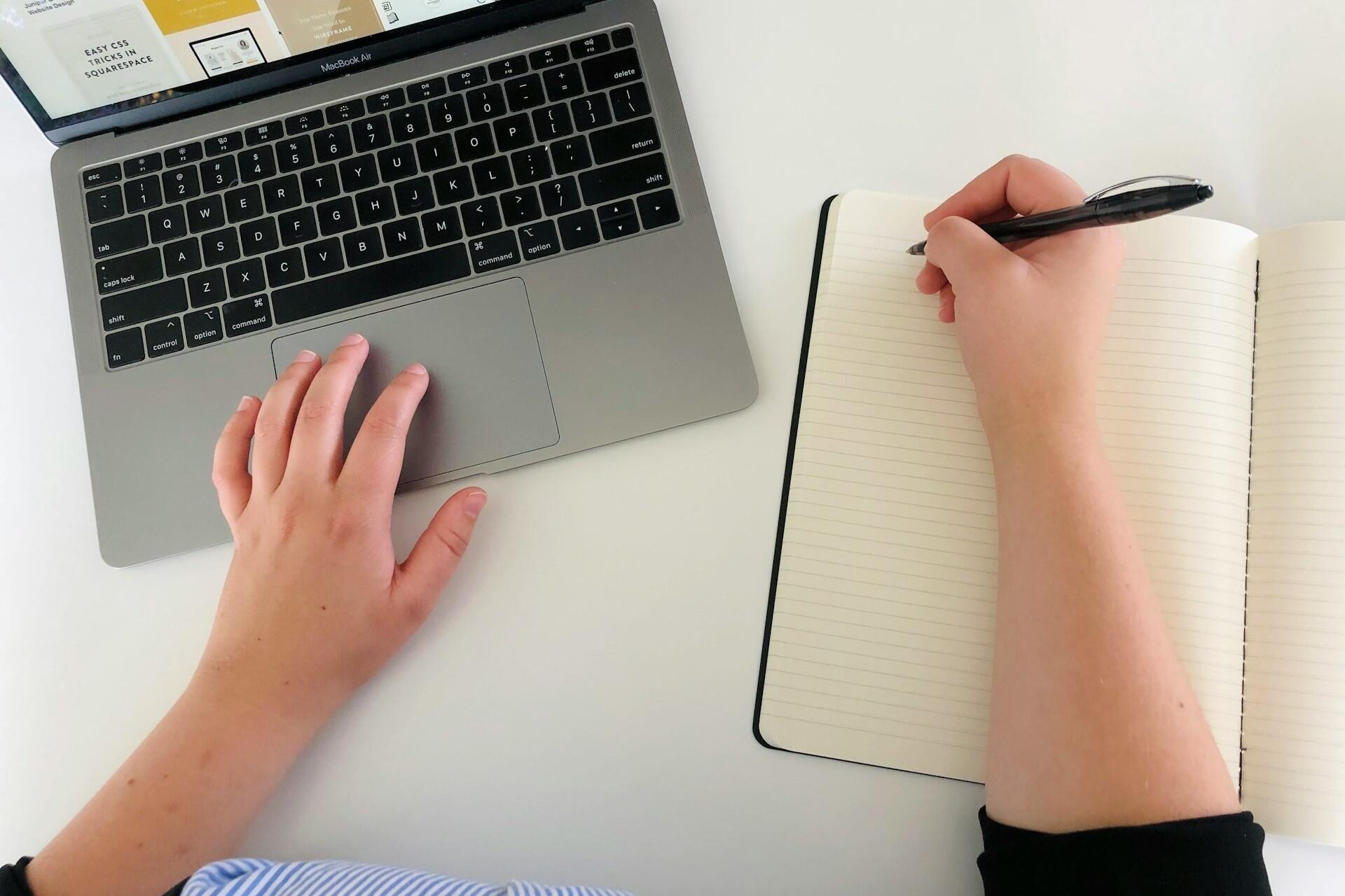 Person using a laptop while taking notes at a desk