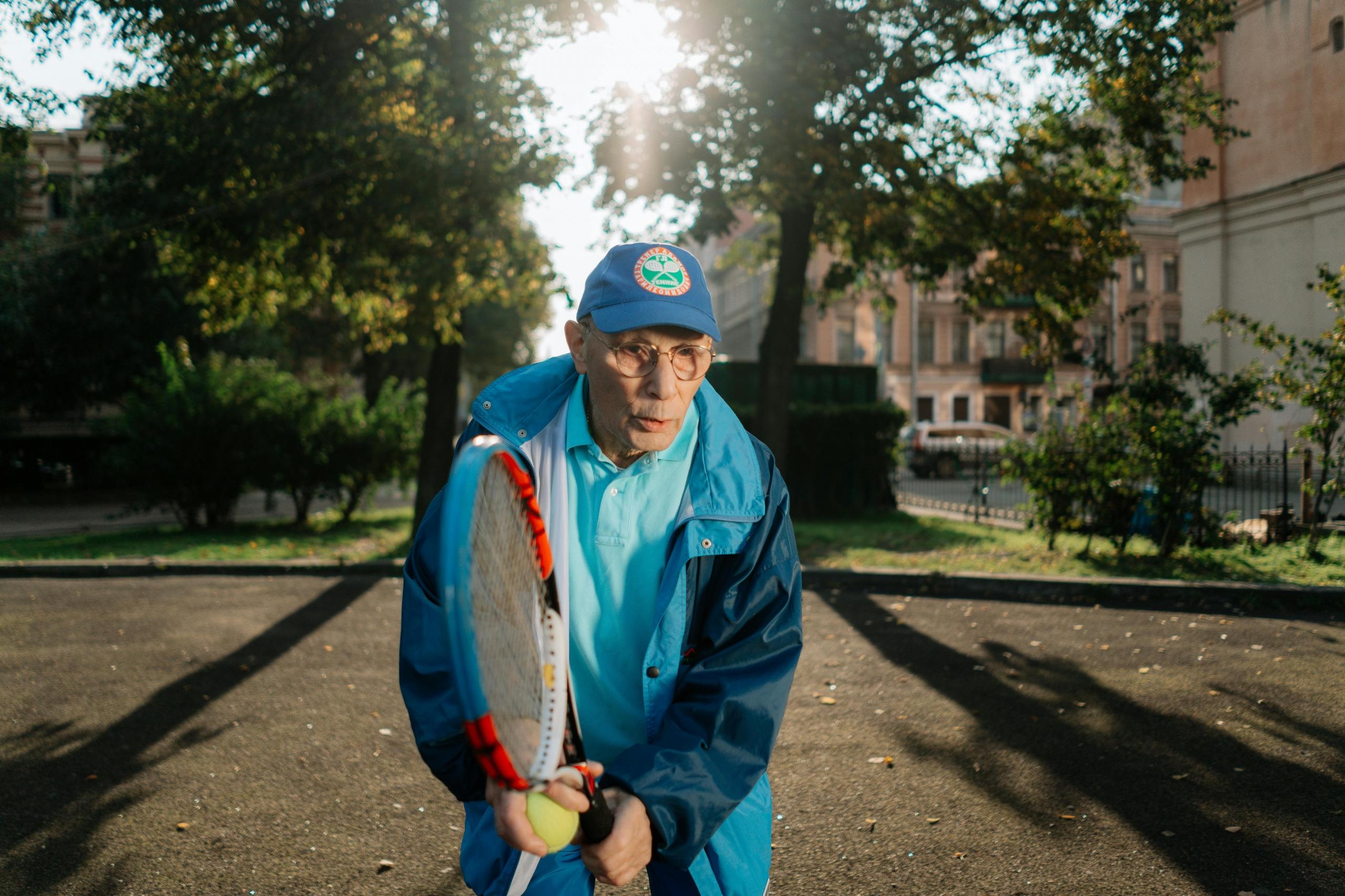 An elderly man getting his exercise in with some tennis lessons.