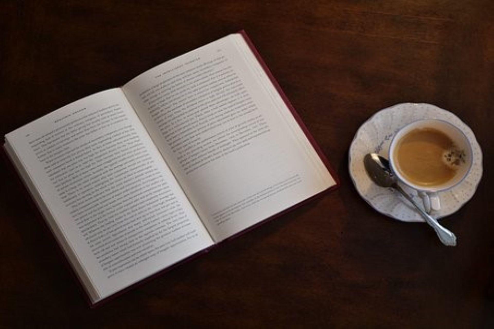 An English book lays open next to a cup of coffee