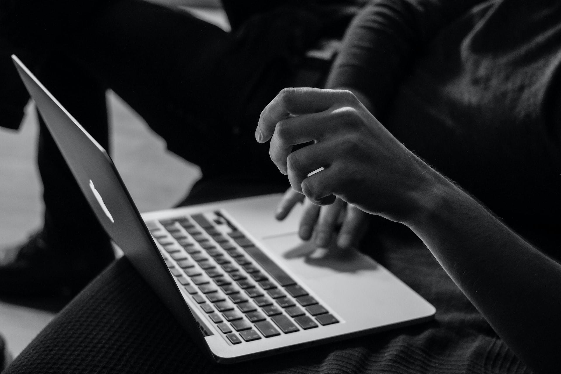 Grayscale photo of a person using a MacBook