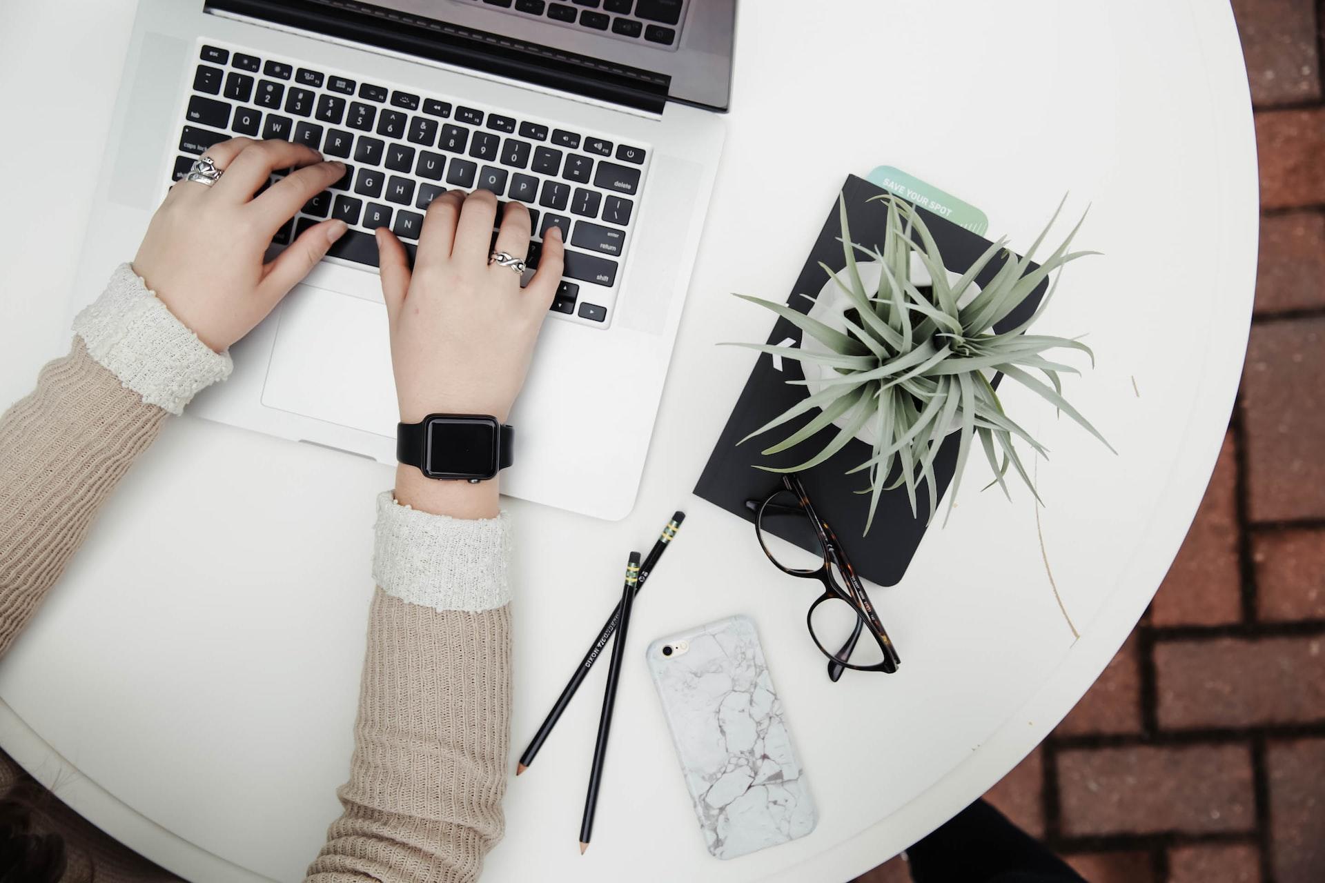 A person using a laptop by a desk plant