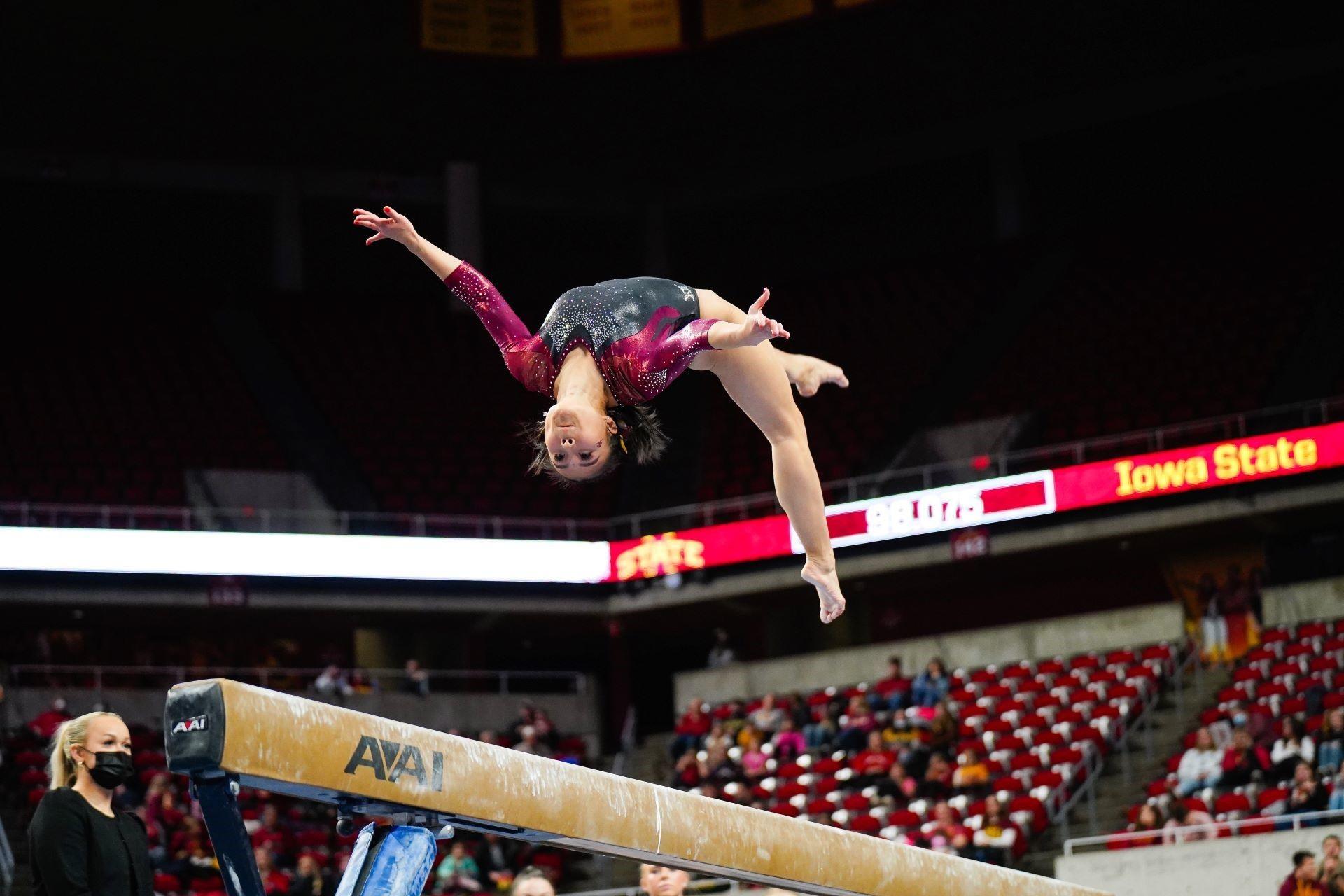 A woman performing gymnastics on a gymnastics beam.