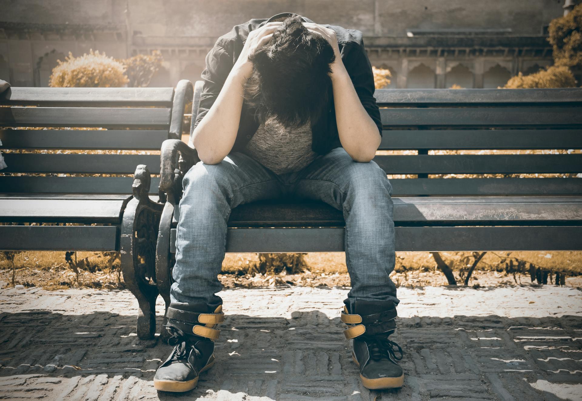 A person sitting on a bench with their head in their hands