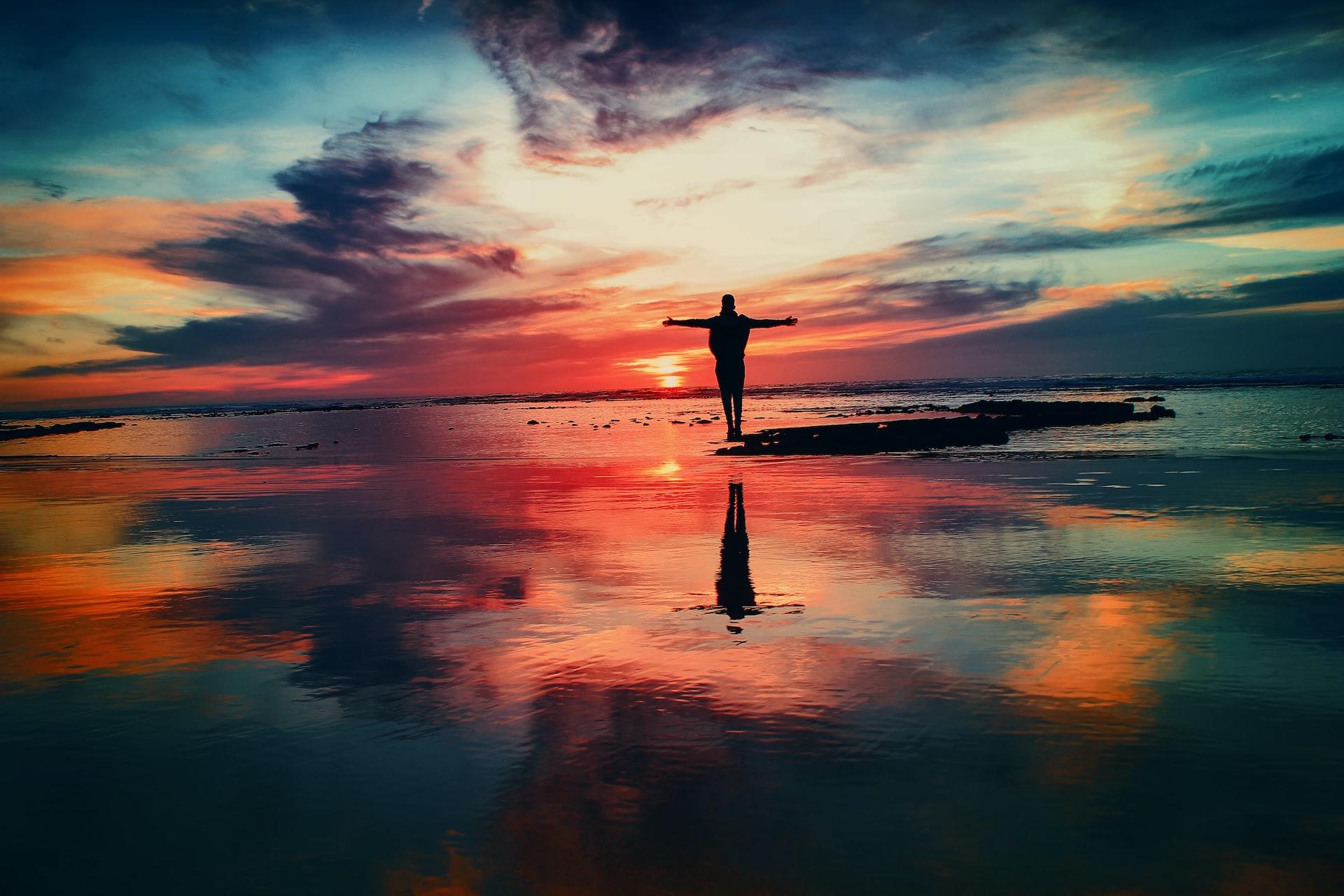 A person standing on a coastline at sunset