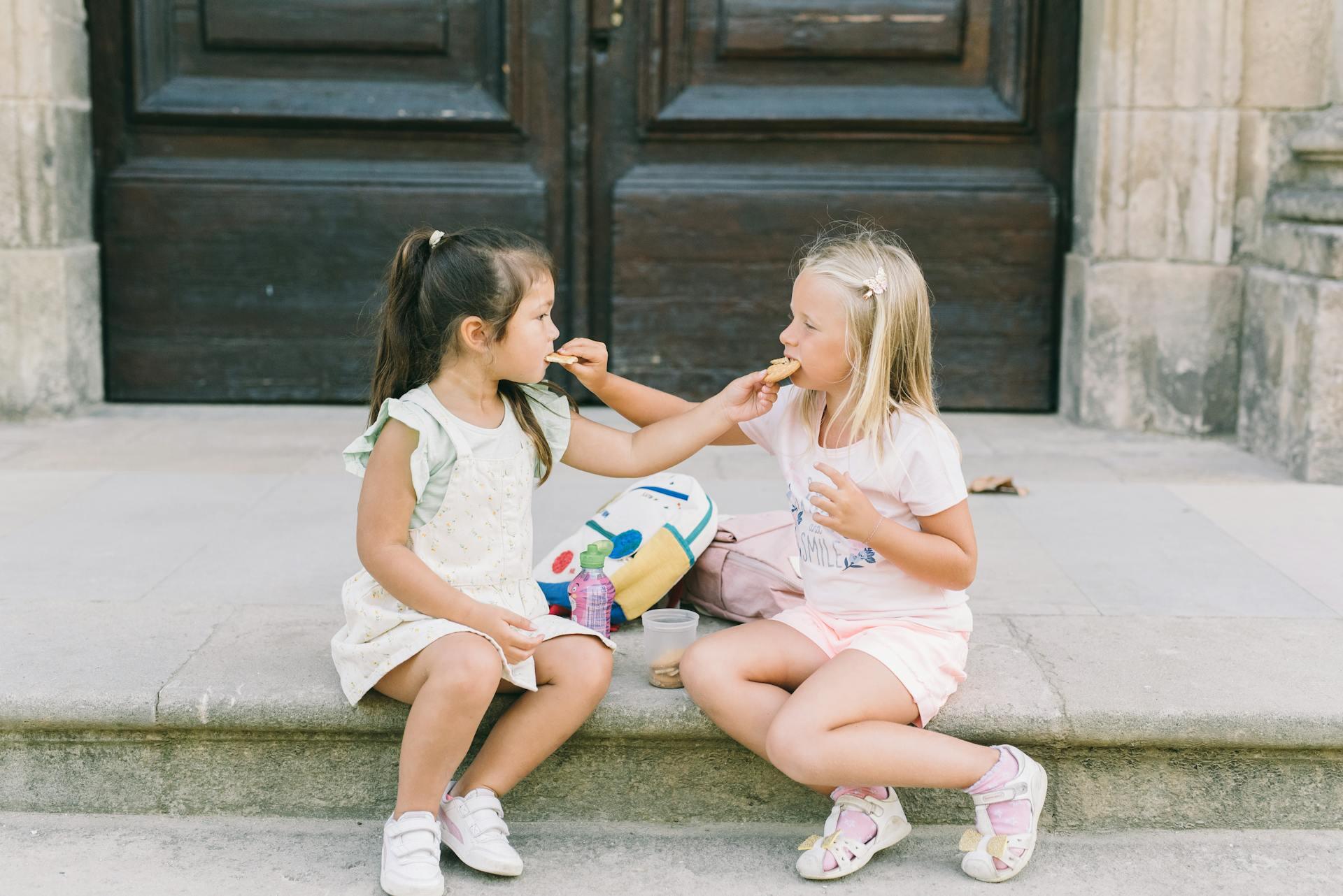 two young girls feeding each other cookies