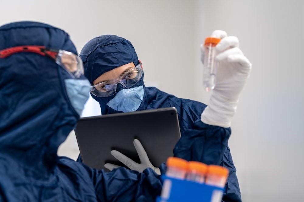 Two people in protective gear analyzing a sample in the test tube.