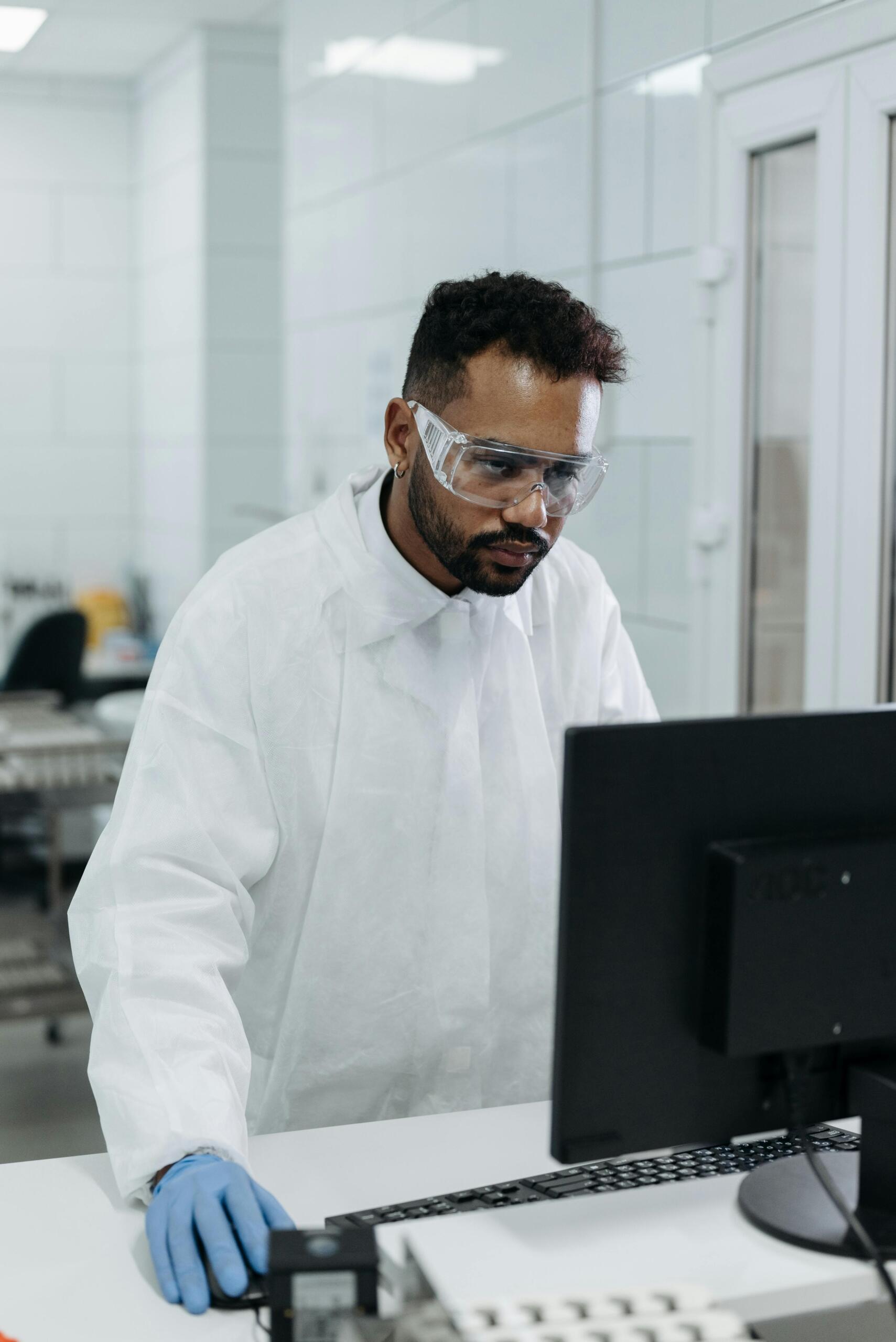 A man in a lab coat working on a computer in a laboratory.