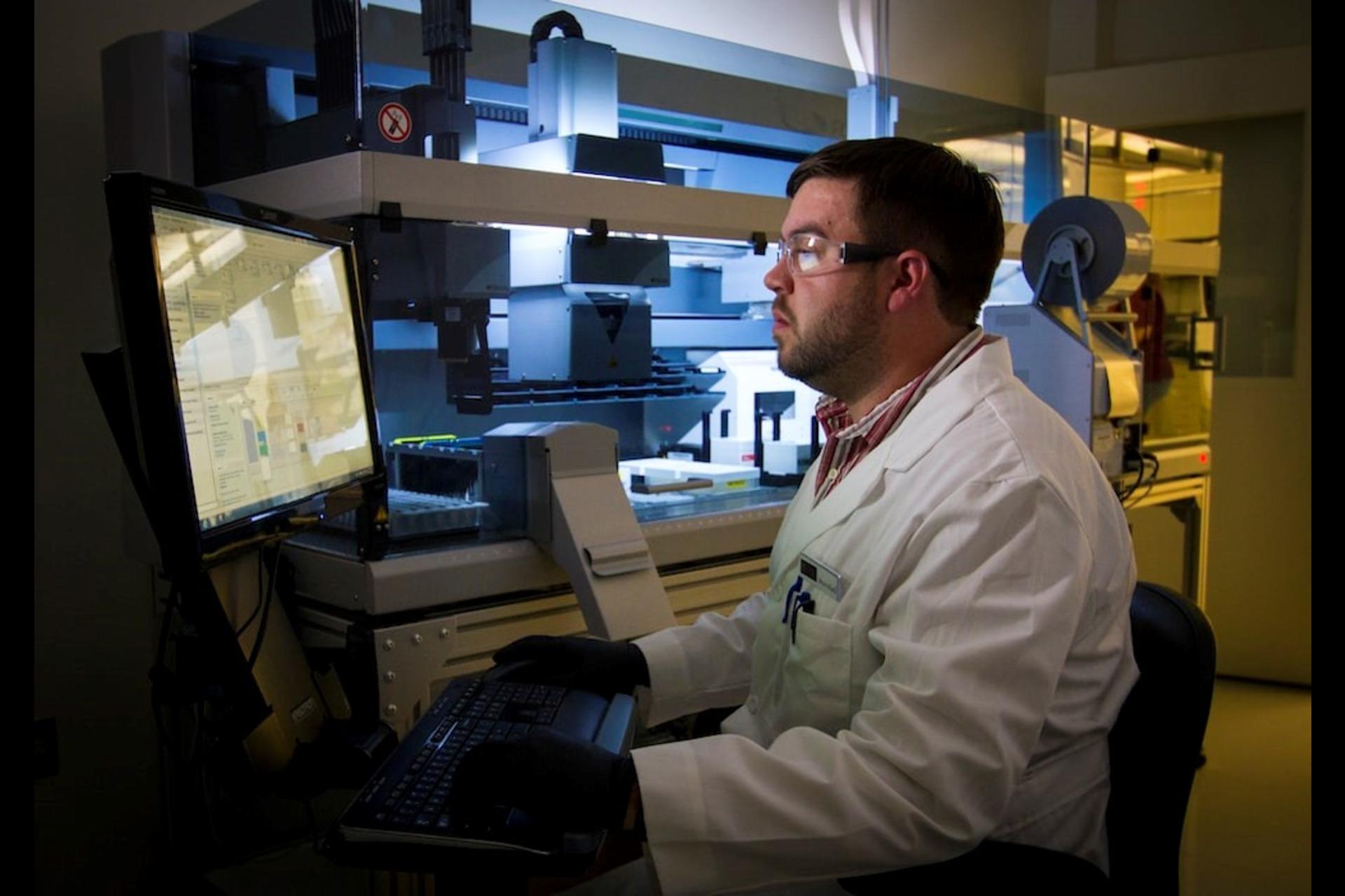 A scientist in a lab coat looking at the test results on a monitor.