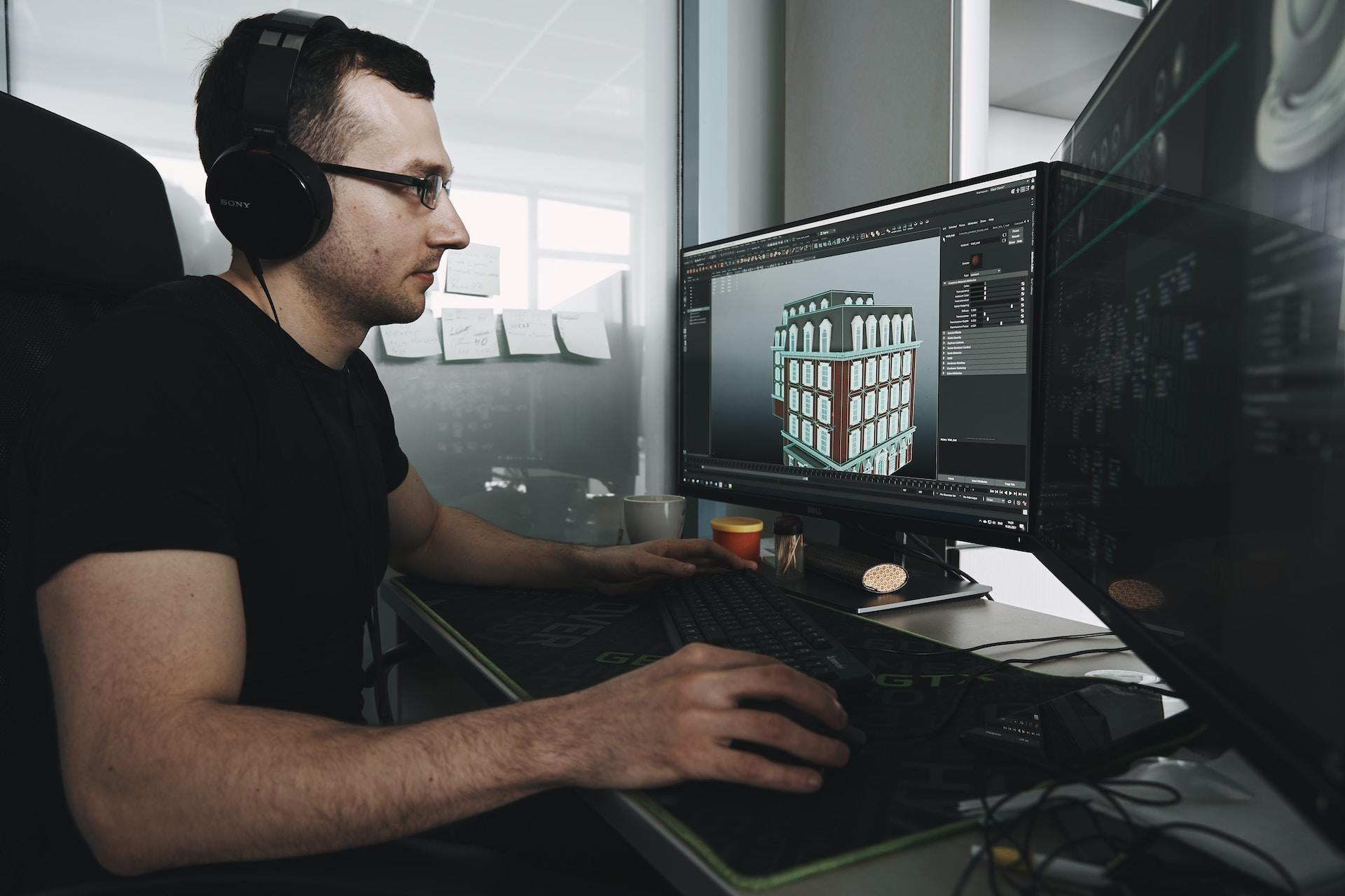 A programmer sits at a computer designing a 3d model of a building