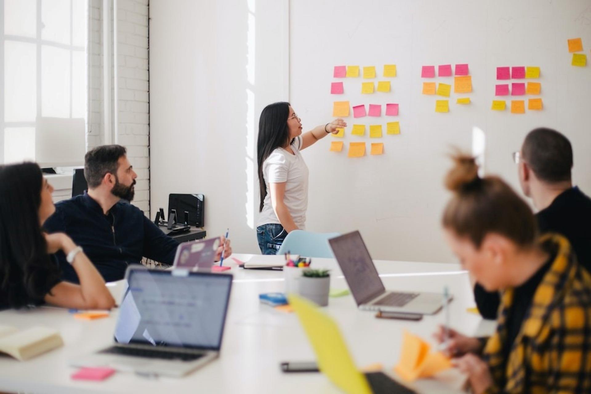 A woman describing the project to colleagues through sticky notes on the wall. 