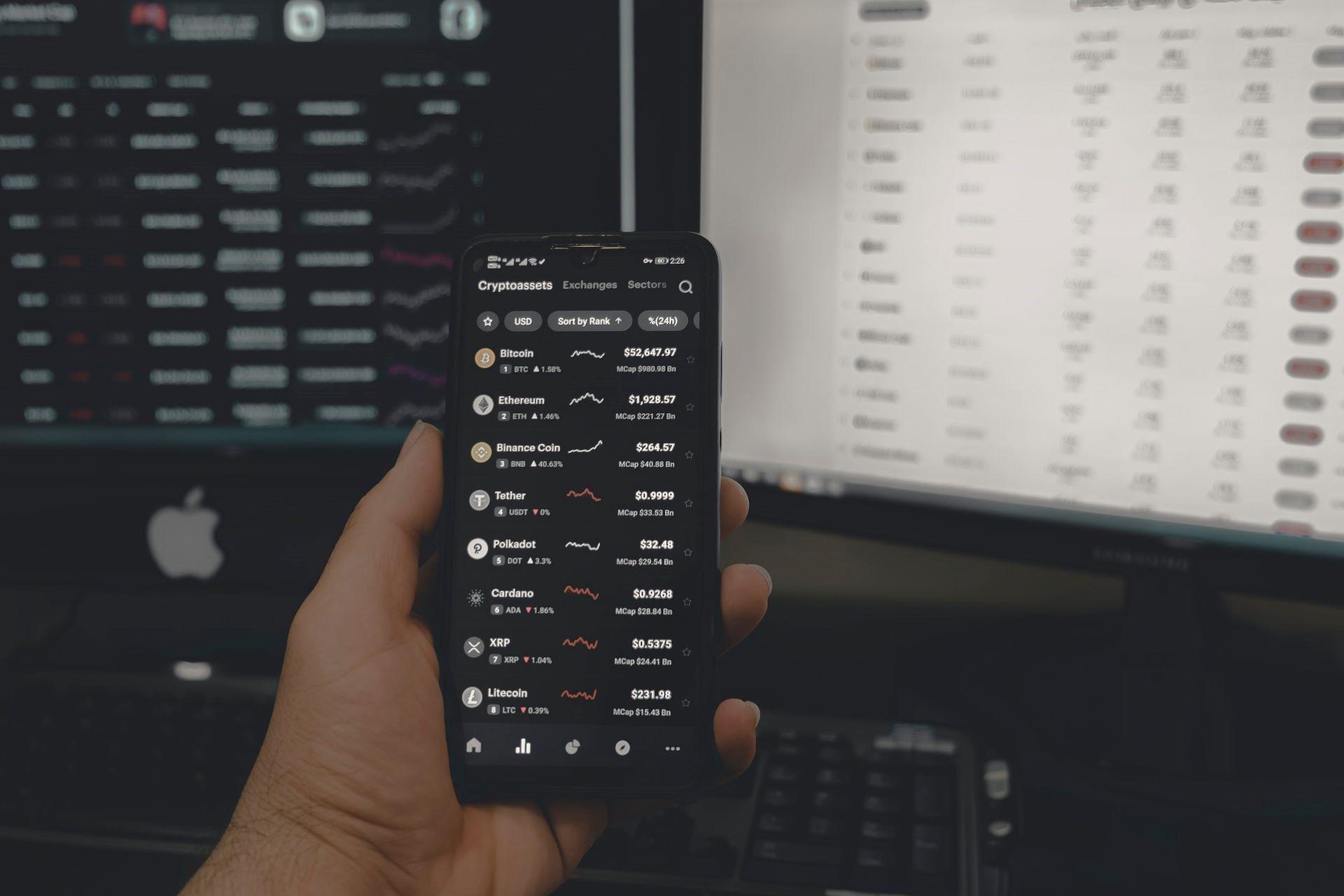 A person trading crypto on a cellphone and laptop.